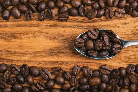 Coffee beans with a spoon close-up scattered on a table made of textured wood Stock Photos