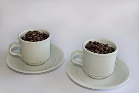 Coffee beans in two coffee cups , on white isolated background. Stock Photos