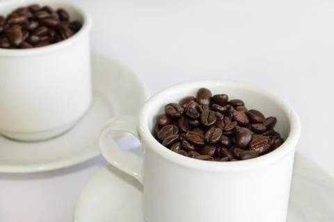 Coffee beans in two coffee cups , on white isolated background.Closeup view. Stock Photos