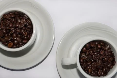 Coffee beans in two coffee cups , on white isolated background.Top view.Macro Stock Photos