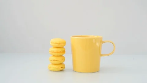 Coffee being poured into a yellow mug next to a stack of yellow macaron cookies Video stock 115939005