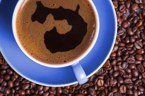 Coffee in blue cup on a table surrounded by coffee beans. Coffee in the shape Stock Photos