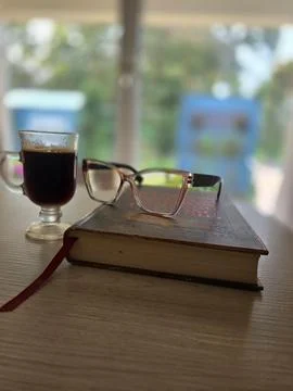 A coffee, a book and glasses on a table Stock Photos