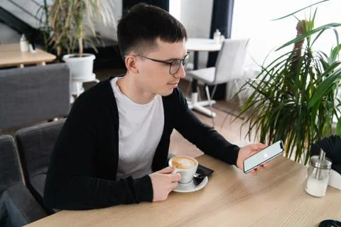 Coffee break. Side view of handsome thoughtful young man holding smart phone and 스톡 사진