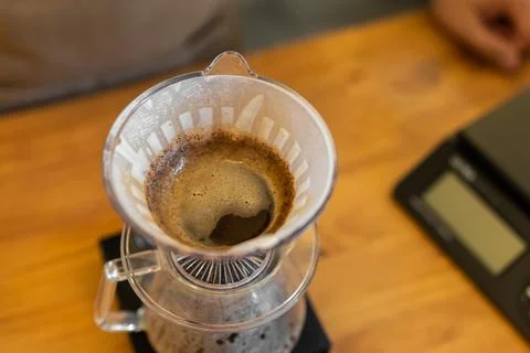 Coffee brewing process with a pour-over dripper on a wooden table. Dark coffee Stockfoto's