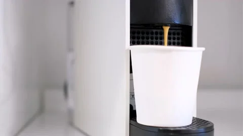 Coffee from a capsule coffee machine is poured into white paper cup close-up. Stock Footage 185014572