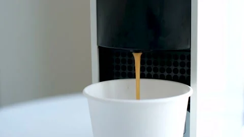 Coffee from a capsule coffee machine is poured into white paper cup close-up. Stock Footage 234492244