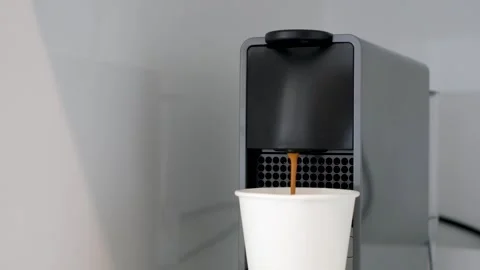 Coffee from a capsule coffee machine is poured into white paper cup close-up. Stock Footage 255990937
