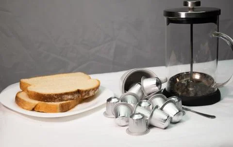 Coffee capsules in falling cup, plate of bread and french press coffee Stock Photos