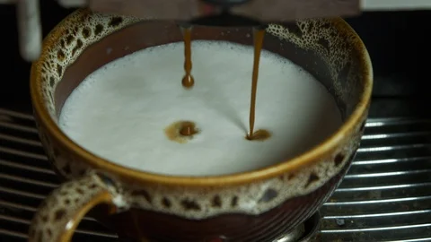 Coffee from a coffee machine is poured into a brown cup with frothy milk Stock Footage 97215343