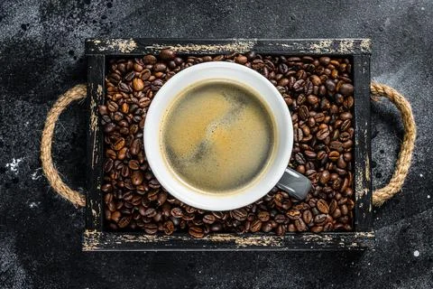 Coffee cup and beans in old wooden tray. Black background. Top view Stock Photos