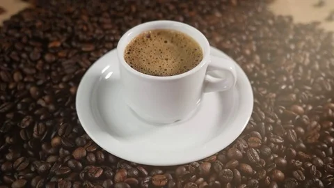 Coffee cup and coffee beans. A white cup of evaporating coffee foam on a table Stock Footage 84746059