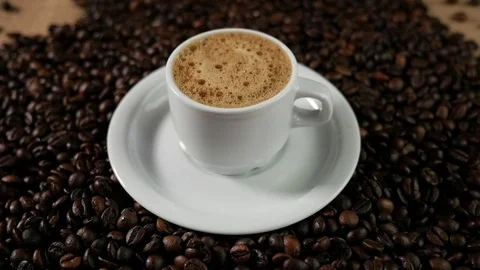 Coffee cup and coffee beans. A white cup of evaporating coffee foam on a table Stock Footage 85031736