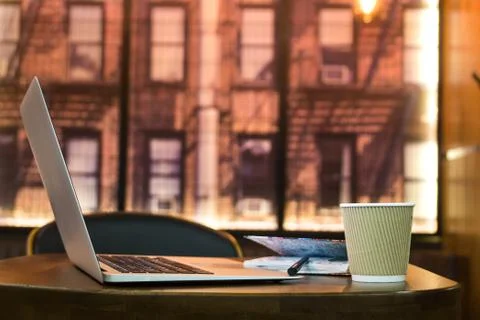 Coffee cup and laptop on the table in cafe. Portable computer, note pad and p Stock Photos