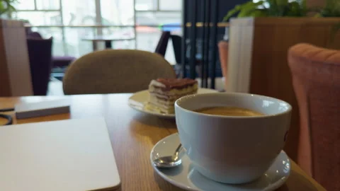 Coffee cup and layered dessert on wooden table in bright cafe lounge with Stock Footage 338134371