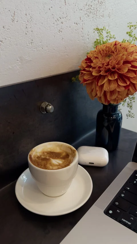 Coffee cup beside orange flower on quiet workspace desk with earbud case and Stock Footage 344967669