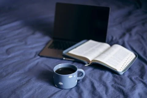 Coffee cup on blue bed with notebook, Bible, laptop and smartphone. Stock Photos