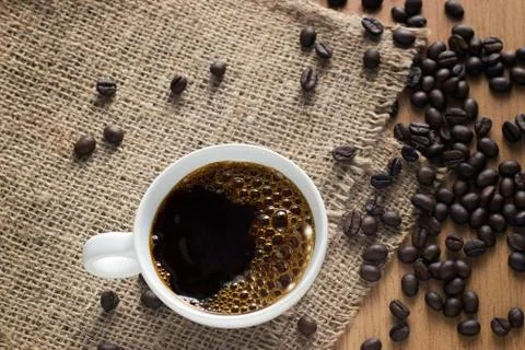 Coffee cup with bubbles and beans on sack background, top view, soft focus Stock Photos