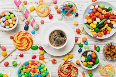 Coffee cup with chocolates and colored candy. Top view on table background wi Stock Photos