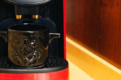Coffee cup with a demon face inside the coffee maker Stock Photos