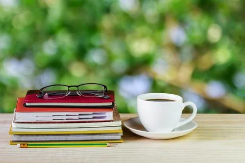 Coffee cup, glasses, and stack of book on wooden table with blur background Foto stock