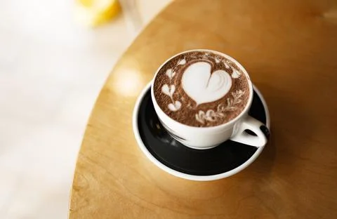 Coffee cup with heart pattern on wooden table in coffee shop Stock Photos