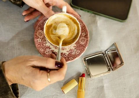 Coffee cup with makeup essentials on a table and hands stirring Stock Photos