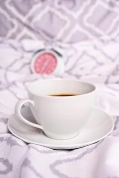 Coffee cup on modern bed sheets with alarm clock in the background Stock Photos