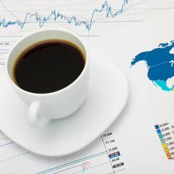 Coffee cup over world map and financial market charts Photos