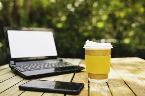 Coffee cup paper with a Computer laptop and phone in green nature backgroun.. Stock Photos