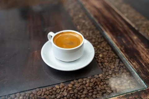 Coffee cup at rustic cafe with interesting table filled with coffee beans Photos
