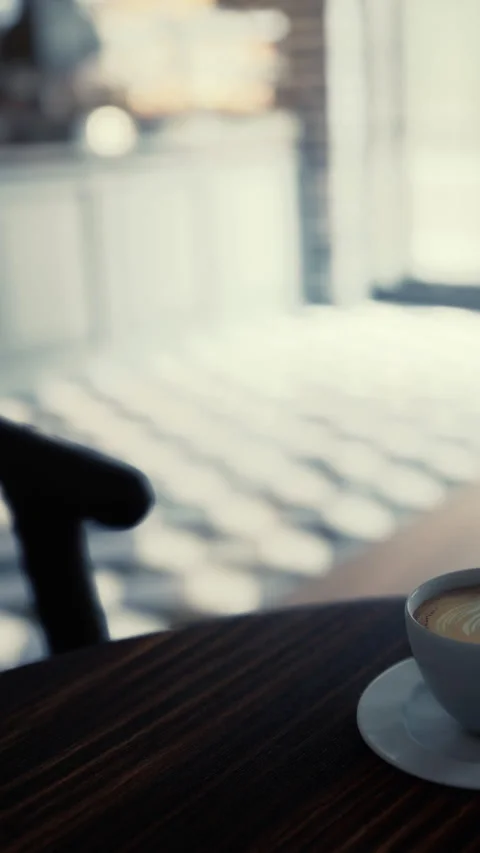 Coffee cup sits on table in cafe with sunlight filtering through window Stock Footage 338350148