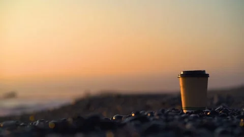 Coffee cup sitting on pebbles beach with sea in background Video stock 133375774