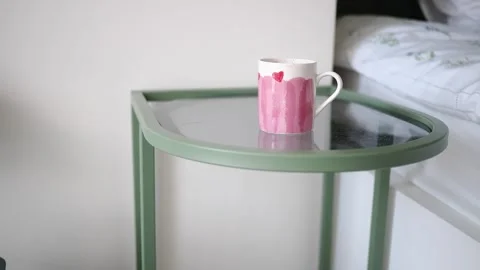 Coffee cup on a small table next to a bed in a room Stock Footage 337810913