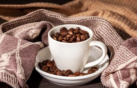Coffee cup surrounded by coffee beans on elegant kitchen linen napkins Stock Photos