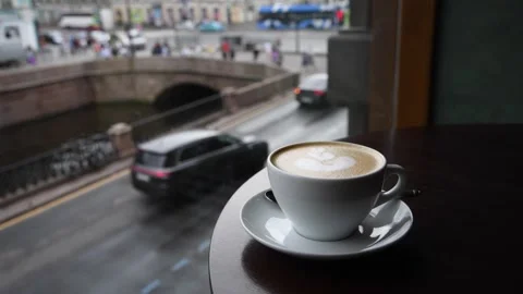 Coffee cup on a table with a rainy city view in the background Video stock 302564182
