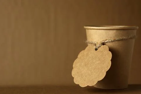 Coffee cup with a tag placed on a plain surface against a brown background in a 스톡 사진