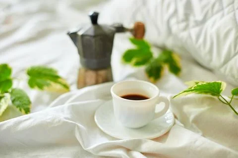 Coffee cup on white bed sheets with geyser coffee maker and green leaves Stock Photos