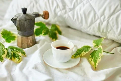 Coffee cup on white bed sheets with geyser coffee maker and green leaves Stock Photos