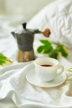 Coffee cup on white bed sheets with geyser coffee maker and green leaves Stock Photos
