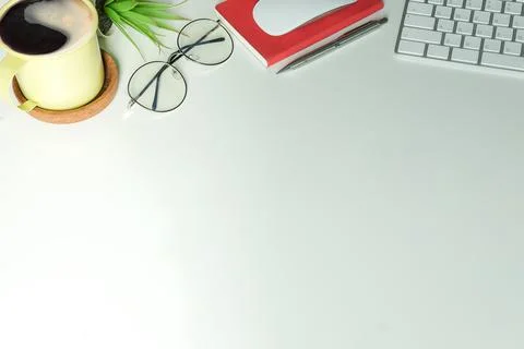 Coffee cup, wireless keyboard, notebook and glasses on white table. Stock Photos