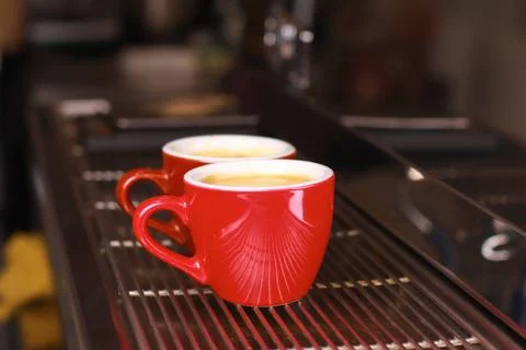 Coffee cups stand inside the coffee machine on a grid, fresh coffee is poured Stock Photos