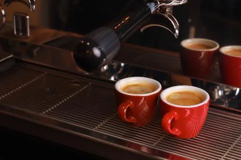 Coffee cups stand inside the coffee machine on a grid, fresh coffee is poured Stock Photos