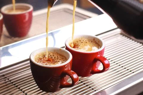 Coffee cups stand inside the coffee machine on a grid, fresh coffee is poured Stock Photos