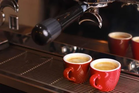 Coffee cups stand inside the coffee machine on a grid, fresh coffee is poured Stock Photos