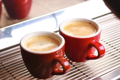 Coffee cups stand inside the coffee machine on a grid, fresh coffee is poured Stock Photos