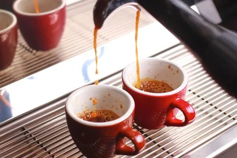 Coffee cups stand inside the coffee machine on a grid, fresh coffee is poured Stock Photos