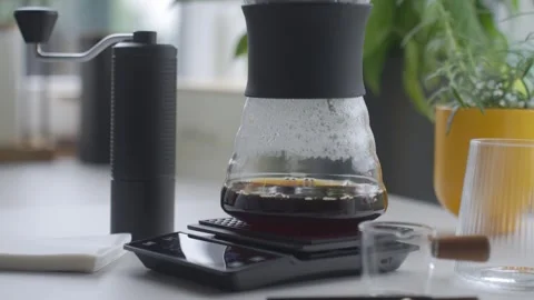 Coffee drips through filter into server on digital scale beside manual grinder Stock Footage 340336047