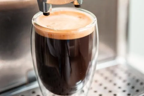 Coffee espresso streaming from coffee machine and pouring into glass. Stock Photos