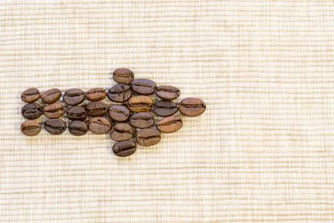 Coffee grains are lined in the form of an arrow on a beige napkin. Stock Photos